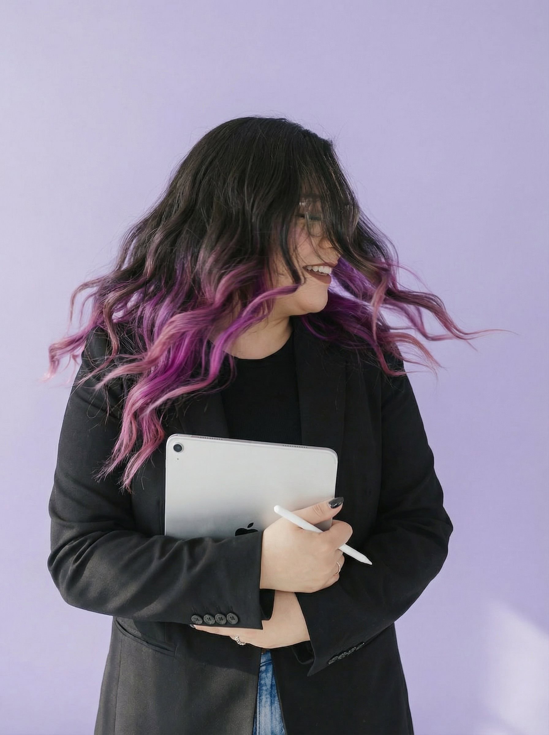 Ingrid in a black blazer holding a tablet and stylus against a lavender wall