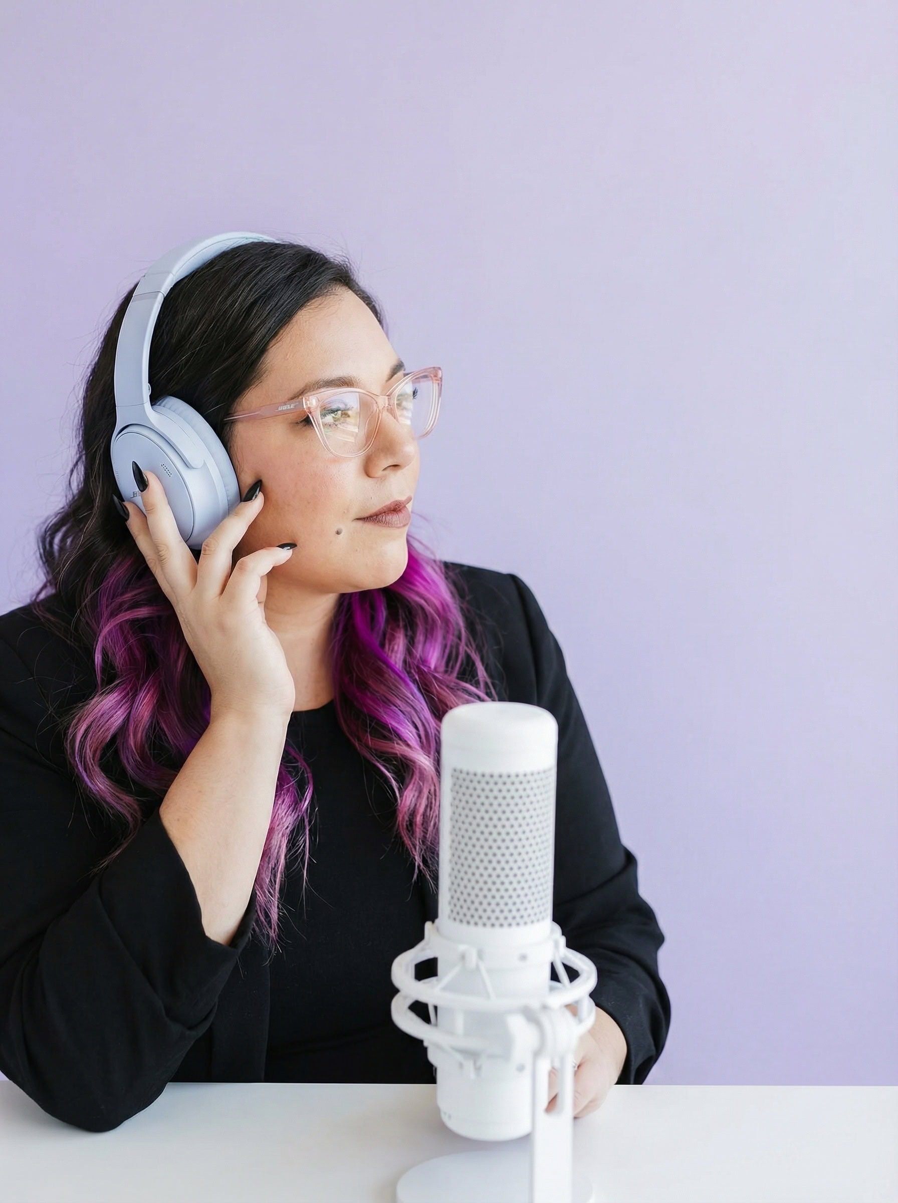 Ingrid in a black blazer wearing headphones beside a white microphone against a lavender wall